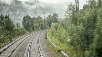 Blick auf eine zweigleisige, elektrifizierte Bahnstrecke, die durch eine neblige, bewaldete Landschaft führt. Korridorsanierungen zwingen Güterzüge teilweise zu langen Umwegen.
