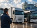 Ein Fuhrparkmanager betrachtet einen Elektro-Lkw und einen Elektrobus vor einem modernen europäischen Verwaltungsgebäude. Das Bild symbolisiert die Auswirkungen neuer EU-Vorgaben auf die Kosten der Verkehrswende.
