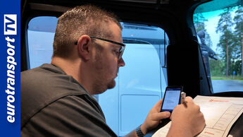 Ein Lkw-Fahrer sitzt in seinem Fahrerhaus, schaut auf sein Smartphone und füllt ein Formular von Fehrenkötter aus, links im Bild das eurotransportTV-Logo.