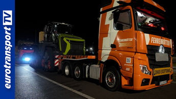 Ein Mercedes-Benz Actros von Fehrenkötter Transport steht nachts mit einem geladenen Claas Xerion auf einem Tiefbettauflieger an einer Raststätte. Links ist das eurotransportTV-Logo zu sehen.