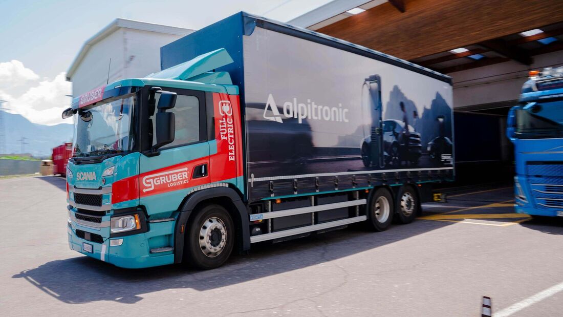 Ein batterieelektrischer Scania-Lkw von Gruber Logistics fährt auf einer Straße zwischen Auer und Bozen und beliefert das Alpitronic-Werk mit Komponenten für Schnellladesysteme.