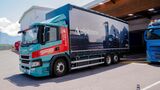 Ein batterieelektrischer Scania-Lkw von Gruber Logistics fährt auf einer Straße zwischen Auer und Bozen und beliefert das Alpitronic-Werk mit Komponenten für Schnellladesysteme.