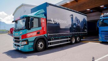 Ein batterieelektrischer Scania-Lkw von Gruber Logistics fährt auf einer Straße zwischen Auer und Bozen und beliefert das Alpitronic-Werk mit Komponenten für Schnellladesysteme.
