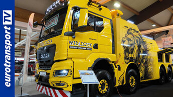 Ein gelber MAN-Berge-Lkw mit Löwen-Motiv auf der IFBA 2025 in Kassel, fotografiert von eurotransportTV – links im Bild das eurotransportTV-Logo.