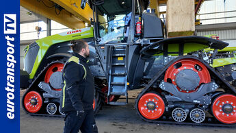 Ein großer Claas Xerion 12.650 mit Raupenlaufwerken steht in einer Werkshalle. Davor blickt ein Mitarbeiter zur Maschine. Links ist das eurotransportTV-Logo zu sehen.