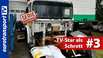 Ein heruntergekommener MAN F8 aus der Serie „Auf Achse“, stark beschädigt und ohne Frontteile, vor Werkstatthallen. Darauf der rote Serien-Stempel, der Text „TV-Star als Schrott #3“ und links das eurotransportTV-Logo.