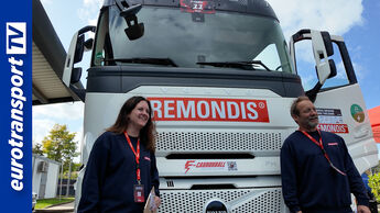 Ein weißer Elektro-Lkw von Remondis steht im Freien. Zwei Personen in blauen Pullovern stehen davor. Links ist das eurotransportTV-Logo zu sehen.