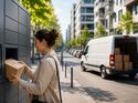 Eine Kundin entnimmt ein Paket aus einer Paketstation, während im Hintergrund ein Pakettransporter in einer Wohnstraße hält. Out-of-Home-Zustellung gewinnt auf der letzten Meile an Bedeutung.