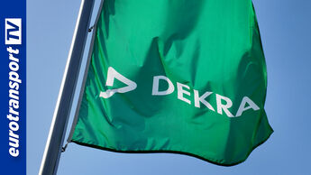 Eine grüne DEKRA-Fahne weht vor blauem Himmel. Das weiße DEKRA-Logo ist gut sichtbar. Die Aufnahme steht symbolisch für das 100-jährige Jubiläum der Prüfgesellschaft. Links im Bild ist das eurotransportTV-Logo.