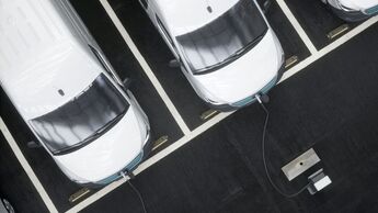 Fleet of generic electric EV delivery vans charging on charging stations