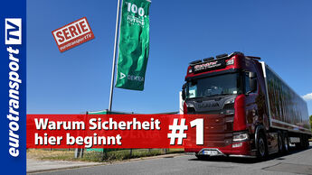 Grüne DEKRA-Jubiläumsflagge mit der Aufschrift „100 Years – Securing the Future“ auf einem Betriebsgelände. Daneben steht ein roter Scania-Lkw. Sichtbar sind das eurotransportTV-Logo, der Serienstempel sowie die Schrifteinblendung „Warum Sicherheit hier beginnt #1“.