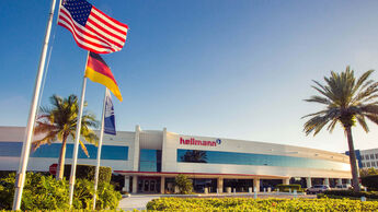 Hellmann-Standort in Miami, Florida, mit drei Flaggen im Vordergrund: der deutschen Nationalflagge, der US-amerikanischen Flagge und der Unternehmensflagge von Hellmann Worldwide Logistics.