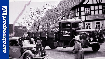 Historisches Schwarz-Weiß-Foto eines Büssing-Lkw der Firma Elflein in einer Dorfstraße der Nachkriegszeit. Im Vordergrund stehen Menschen und Pkw, links das eurotransportTV-Logo.