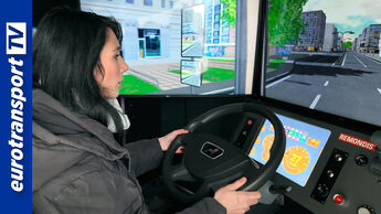 Junge Frau sitzt in einem REMONDIS-Fahrsimulator und steuert ein virtuelles Lkw-Fahrzeug, auf den Monitoren vor ihr ist eine Stadtumgebung zu sehen. Links im Bild ist das eurotransportTV-Logo eingeblendet.