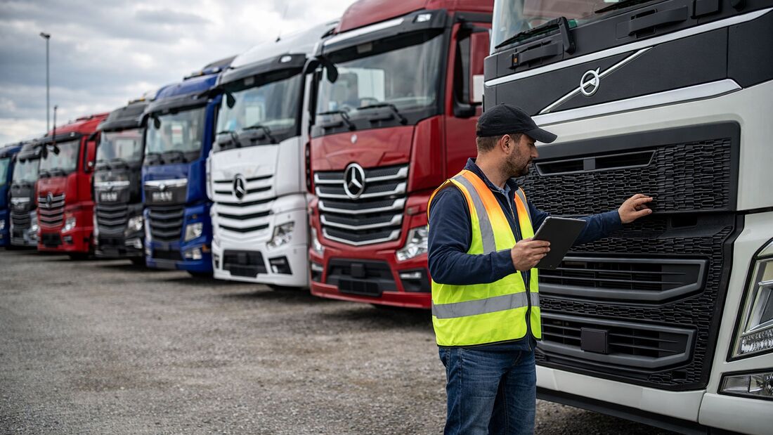 Käufer prüft gebrauchten Lkw auf Händlerhof mit mehreren abgestellten Nutzfahrzeugen