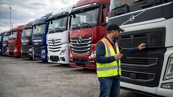 Käufer prüft gebrauchten Lkw auf Händlerhof mit mehreren abgestellten Nutzfahrzeugen