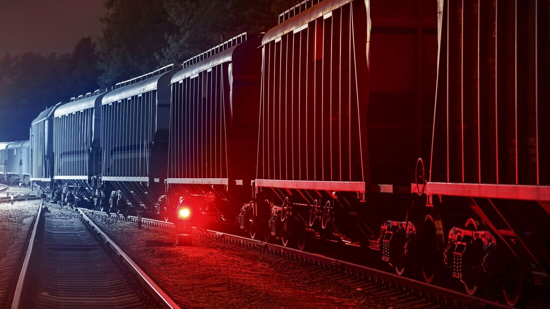 Large cargo train with goods leaving the terminal at night, wagons (containers) close-up. Concept urban scene. Illumination, red light. Freight transportation, industry, business, logistics, delivery