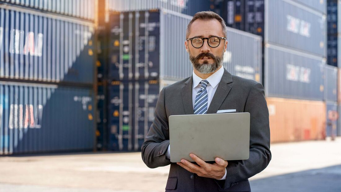 Logistiker mit Laptop vor Containern