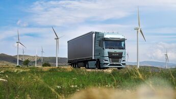 MAN Lkw fährt durch eine Landschaft mit Windrädern.