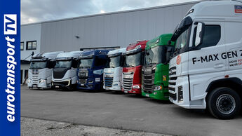 Mehrere Lkw stehen vor einer Halle in Reihe, rechts vorn ein weißer Ford F-MAX Gen 2.0. Links ein blauer Balken mit eurotransportTV-Logo.