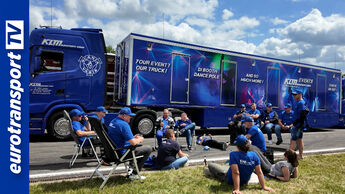 Mehrere Mitarbeiter einer Spedition sitzen und liegen entspannt vor einem blauen Lkw von KLM Transporte mit Event-Auflieger, darüber ein heller Himmel mit Wolken, links das eurotransportTV-Logo sichtbar.