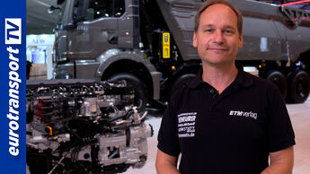 Moderator von eurotransportTV auf der IAA Transportation vor einem schweren Lkw und ausgestellter Nutzfahrzeugtechnik, eurotransportTV-Logo links.