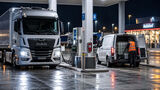 Nächtliche Szene an einem Autohof mit Lkw und weißem Transporter, in dessen Laderaum sich ein großer Dieselbehälter befindet.