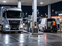 Nächtliche Szene an einem Autohof mit Lkw und weißem Transporter, in dessen Laderaum sich ein großer Dieselbehälter befindet.