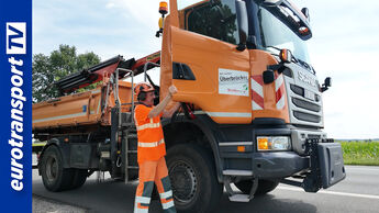Orange-farbiger Lkw von Straßen NRW in Seitenansicht mit einem vor dem Lkw stehenden Mitarbeiter.