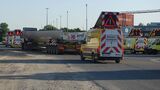 Schwertransport mit einem großen Industriebauteil auf einem Tieflader, begleitet von mehreren gelben Sicherungsfahrzeugen mit Warnleuchten und Schwertransport-Kennzeichnung.