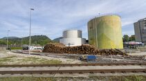 Silos mit Holzstapeln im Vordergrund und Schienen