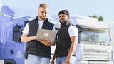 Truckers collaborating on logistics management using laptop. Two male truckers discussing transport routes and fleet details using a laptop at a truck parking lot, ensuring efficient delivery