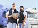 Truckers collaborating on logistics management using laptop. Two male truckers discussing transport routes and fleet details using a laptop at a truck parking lot, ensuring efficient delivery
