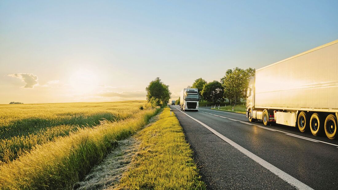 Trucks moving against each other on the road at sunset.