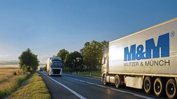 Trucks moving against each other on the road at sunset.