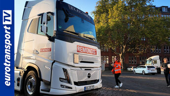 Weiße Volvo-FH-Aero-Electric-Zugmaschine mit Remondis-Logo im Vordergrund; rechts gehen Janina Thielmann und Andreas Abraham in orangefarbener Arbeitskleidung. Links ist das eurotransportTV-Logo zu sehen.