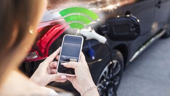 Woman using smart phone while standing by charging electric car