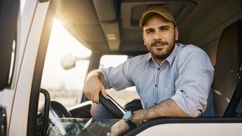 Young truck driver behind steering wheel in vehicle cabin looking at camera.