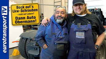 Zwei Lkw-Mechaniker stehen Arm in Arm in einer Werkstatt und lächeln selbstbewusst in die Kamera. Beide tragen blaue Arbeitskleidung, der rechte Mann hat eine dunkle Kappe auf. Im Hintergrund sind Werkstattausrüstung, ein Lkw-Heck und weiße Fahrzeugteile zu sehen. Links im Bild befindet sich ein gelbes Schild in der Form eines Verkehrsschilds mit der Aufschrift: „Bock auf’s Lkw-Schrauben – nicht auf Labern? Dann Auto Obermann!“ Am linken Bildrand ist das blau-weiße eurotransportTV-Logo zu sehen.