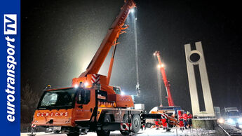 Zwei große Autokrane heben bei Nacht im Schneetreiben eine DDR Begrüßungsstele am ehemaligen Grenzübergang Marienborn ab. Mehrere Arbeiter in Warnkleidung stehen neben der Stele. Links am Bildrand ist das Logo von eurotransportTV eingeblendet.